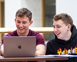 picture of two male students smiling and looking at a macbook screen